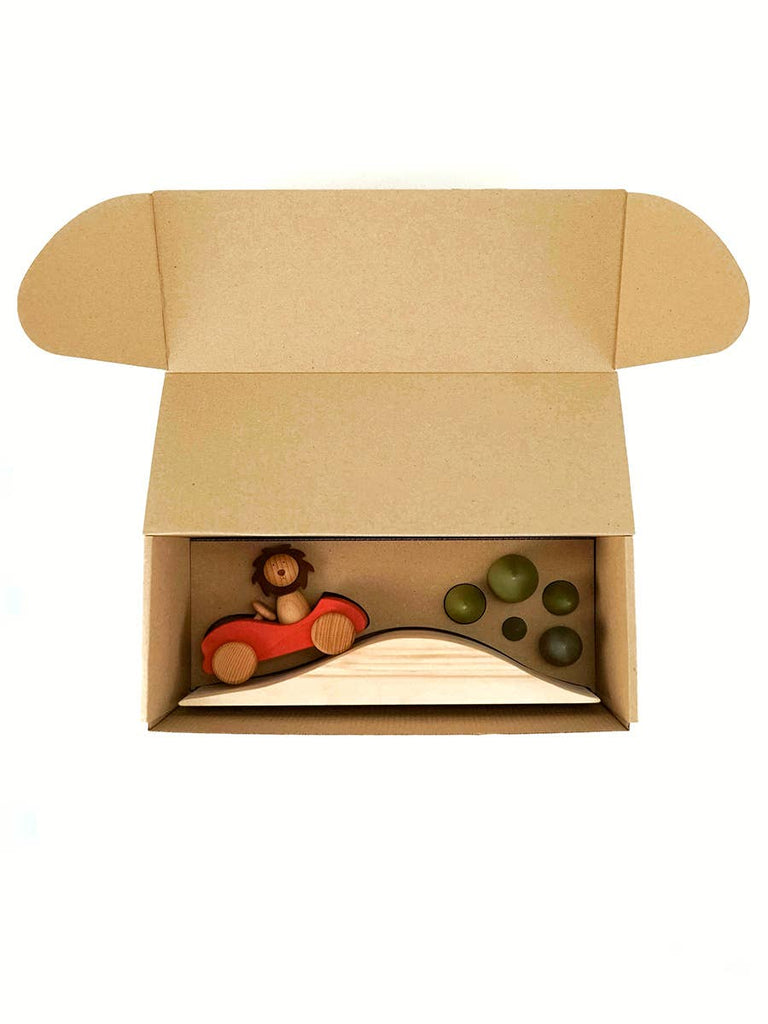 Open cardboard box with Sabo Concept First Journey: includes a small wooden toy lion in a red car, a curved ramp, and three green balls—perfect for imaginative, open-ended play.