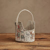 The Coral & Tusk Easter Parade Basket, featuring a scalloped edge, handle, and embroidered animals and children, rests on a rustic wooden surface against a neutral textured background.