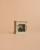 The Maileg Fireplace, Mouse Size - Off White is centered against a plain peach background, its small white wooden frame with a vintage finish and miniature logs inside evoking the charm of a cozy miniature home.