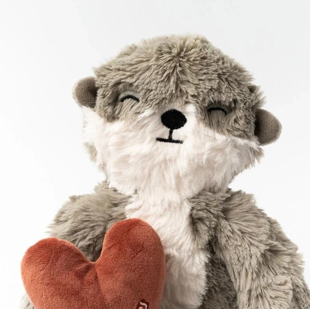 Plush toy otter with a cheerful expression, holding a red heart, filled with hypoallergenic fiberfill, against a plain white background.