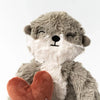 Plush toy otter with a cheerful expression, holding a red heart, filled with hypoallergenic fiberfill, against a plain white background.