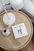A round wooden bedside table holds a white lamp, a small vase with dried plants, and the Black and White Contrast Book for Baby—featuring high-contrast images including a zebra on the cover—perfect for supporting visual development.