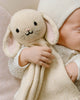 A baby dressed in cream cuddles the Cuddle + Kind Organic Cotton Baby Bunny Lovey (Oatmeal), featuring embroidered eyes, nose, and whiskers—a soft, fair trade toy that makes an adorable gift.