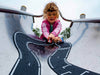 A young child in a pink jacket plays with cars on the Large Flexible Toy Race Track - Grand Prix, designed to look like a racetrack, as seen from the bottom of the slide looking up.