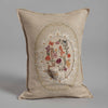 The Sugar Egg Pocket Pillow is a beige pillow adorned with intricate embroidery of colorful flowers, mushrooms, and a small bear. It evokes an Easter wonderland and features an elegant design framed by an embroidered metallic gold leaf border.