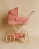 The Konges Sloejd Doll Pram - Bubblegum Check features red and white quilted fabric, a beige frame, four large wheels, a matching storage basket, and a padded mattress, all set against a beige background.