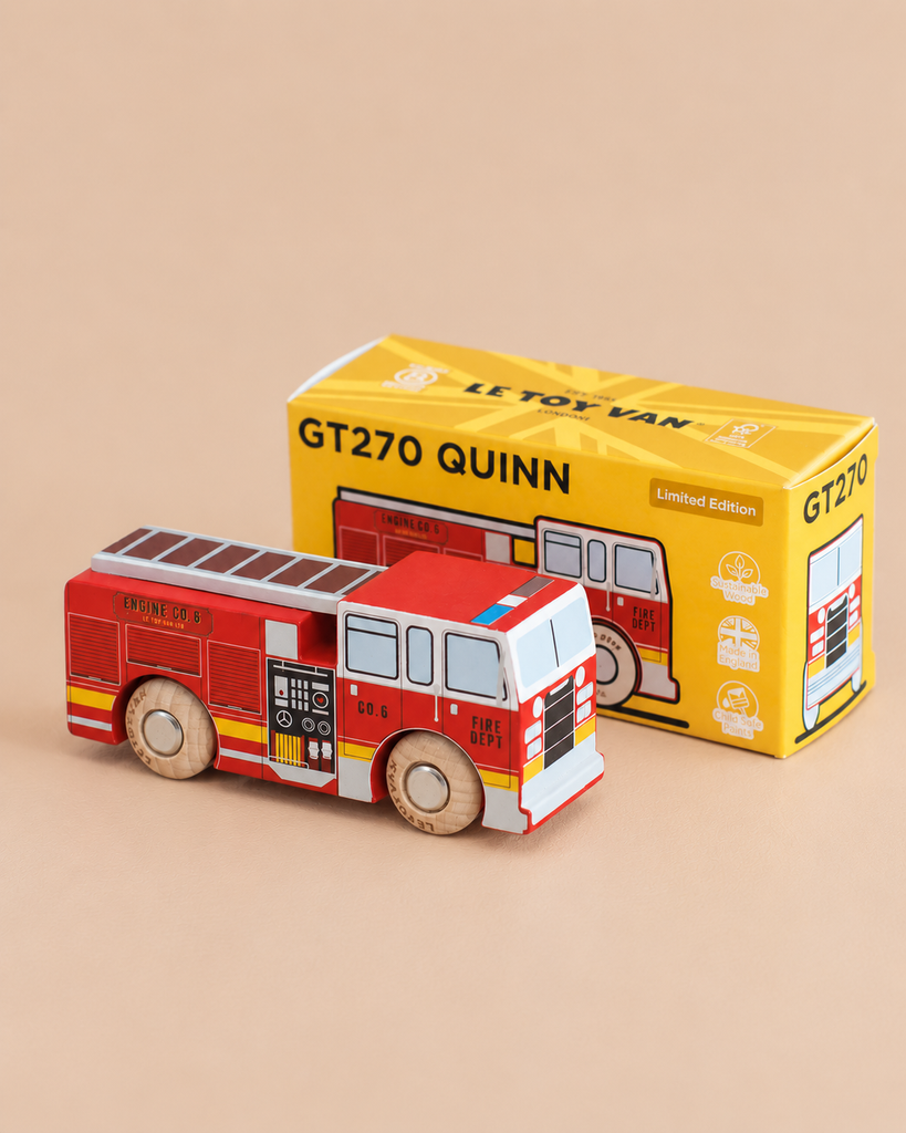 A small wooden fire engine, No. 44 GT270 Quinn, sits in front of its yellow box labeled “Made in England.” The red rescue toy features white and black details for imaginative play, and its packaging displays an illustration that matches the toy inside.