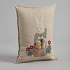 The Easter Bunny Pocket Pillow showcases an embroidery of the Easter Bunny in a blue outfit with a basket and two smaller rabbits, surrounded by red and blue flowers on light fabric—ideal for decoration.