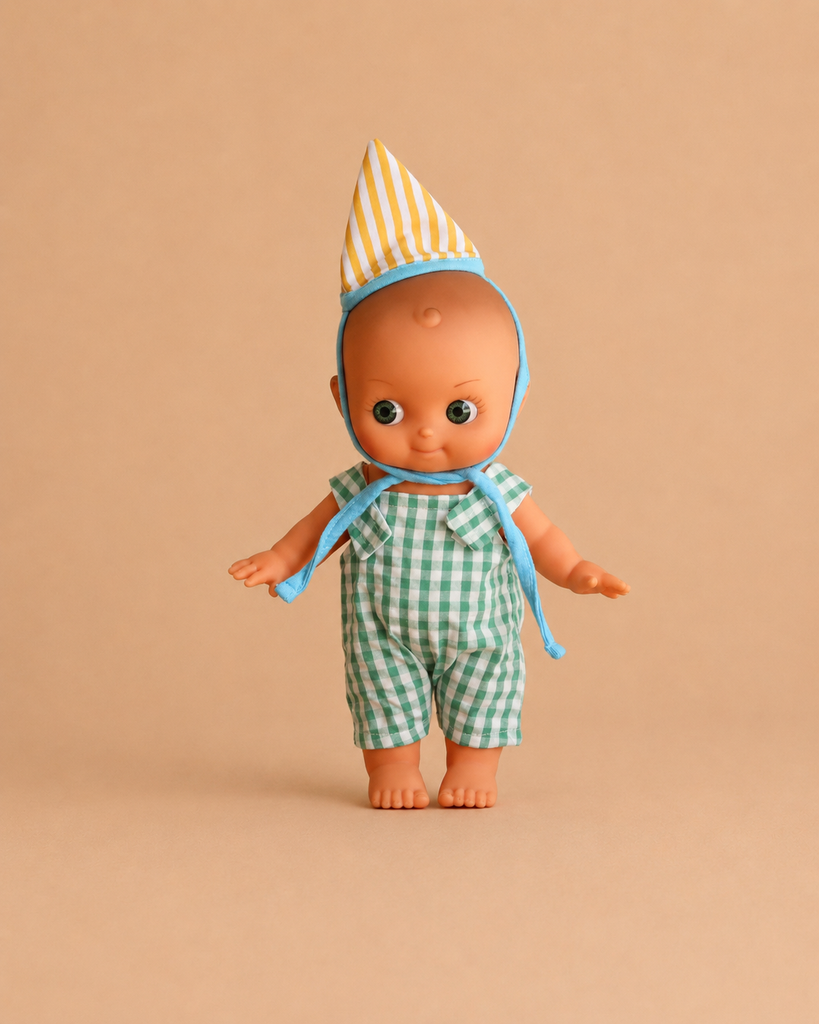 The Mini Pancha Doll - Zebulon with Green Gingham Birthday Outfit stands against a plain beige background, dressed in charming green gingham overalls and a yellow-striped party hat. Crafted from high-quality vinyl, this doll is perfect for imaginative play.