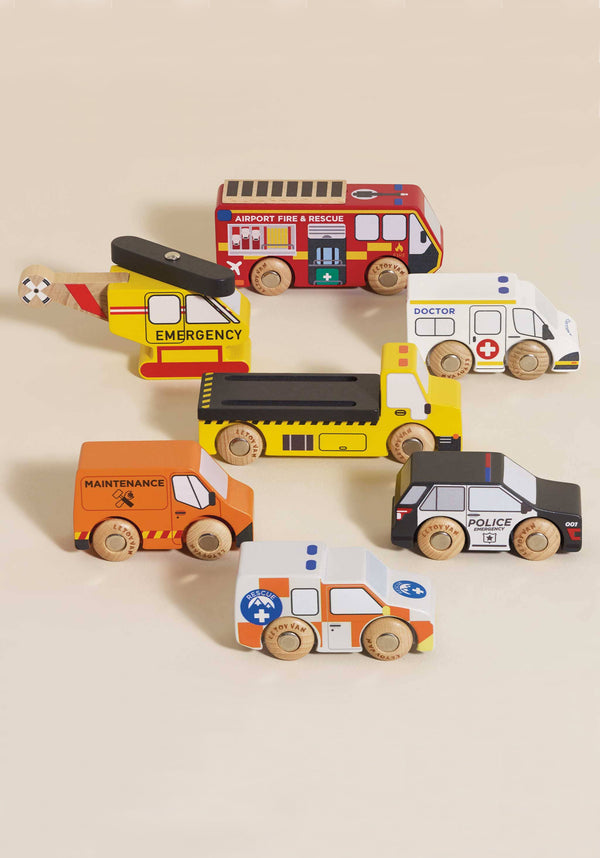 The Emergency Helicopter & Rescue Cars set features seven colorful FSC-certified wooden vehicles—fire truck, police car, ambulance, doctor's van, maintenance van, tow truck, and helicopter—arranged on a light surface.