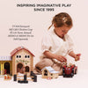 A young girl plays on the floor with the Farmyard Tractor & Trailer, a wooden set featuring a barn, animals, and a magnetic trailer. The text above says, "Inspiring imaginative play since 1995." Model numbers are shown on the left.