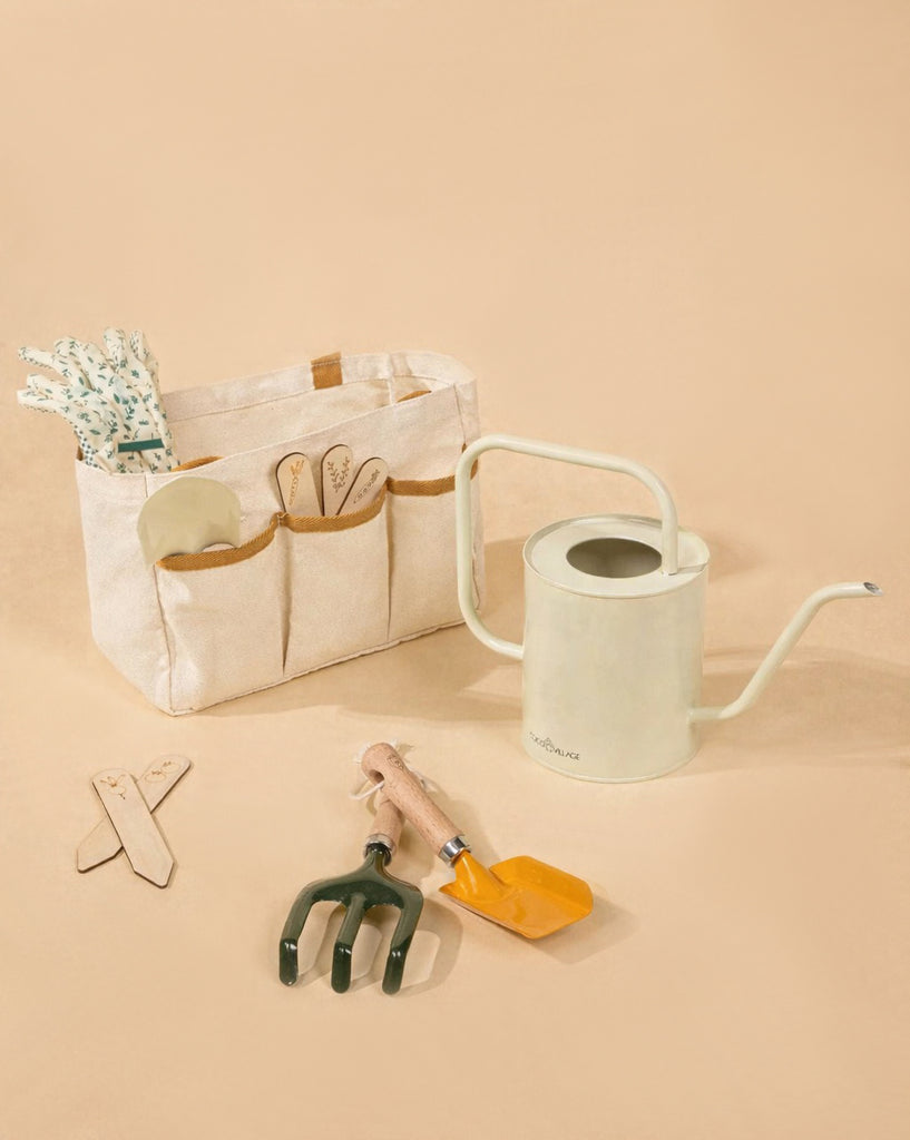 The Gardening Tools Playset includes a beige gardening tote filled with child-friendly tools, a pale watering can, green hand cultivator, orange trowel, and two plant markers—perfect for kids—displayed on a light beige background.