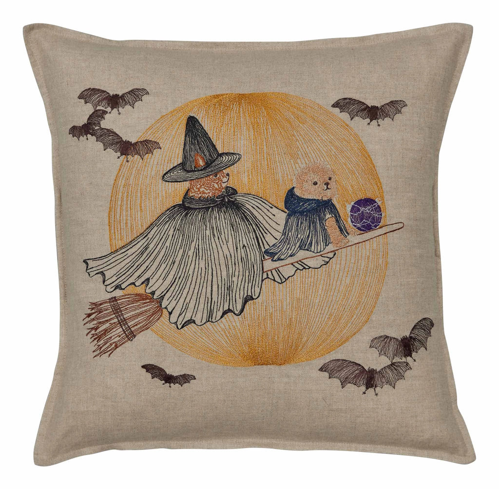 The Coral & Tusk Supermoon Spell Pillow showcases an embroidered witch in a tattered cape and pointed hat holding a broomstick, riding alongside a small, caped Wizard Puppy on another broomstick. They are surrounded by flying bats set against a circular, orange background.