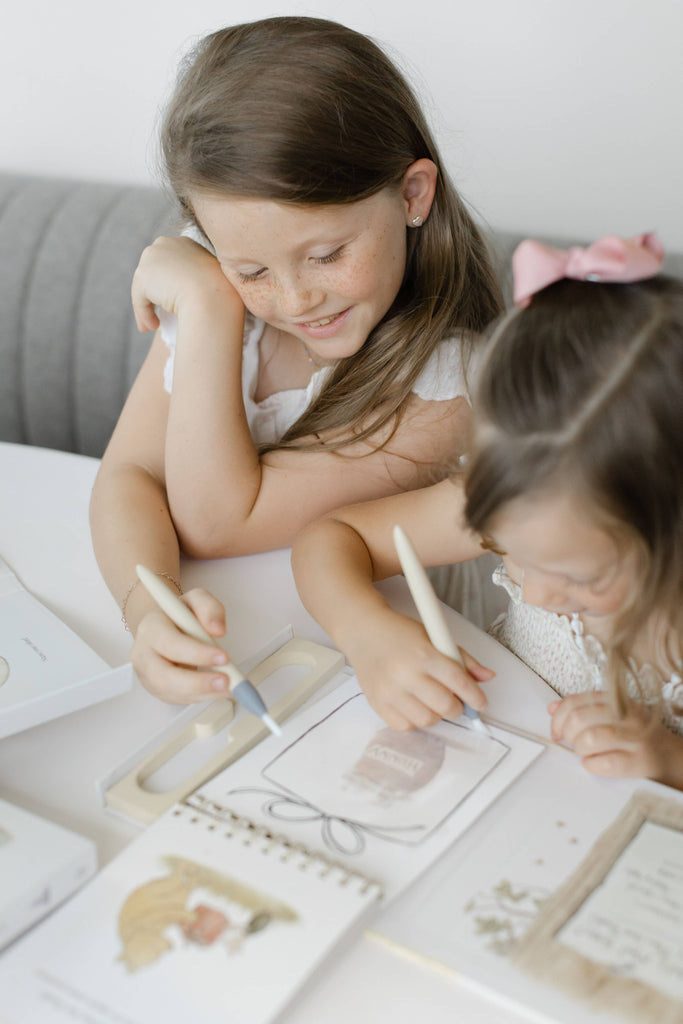 Two girls use water-reveal pens to color illustrations in a Winnie-the-Pooh: Pooh’s Birthday Surprise (Water Reveal) activity book.