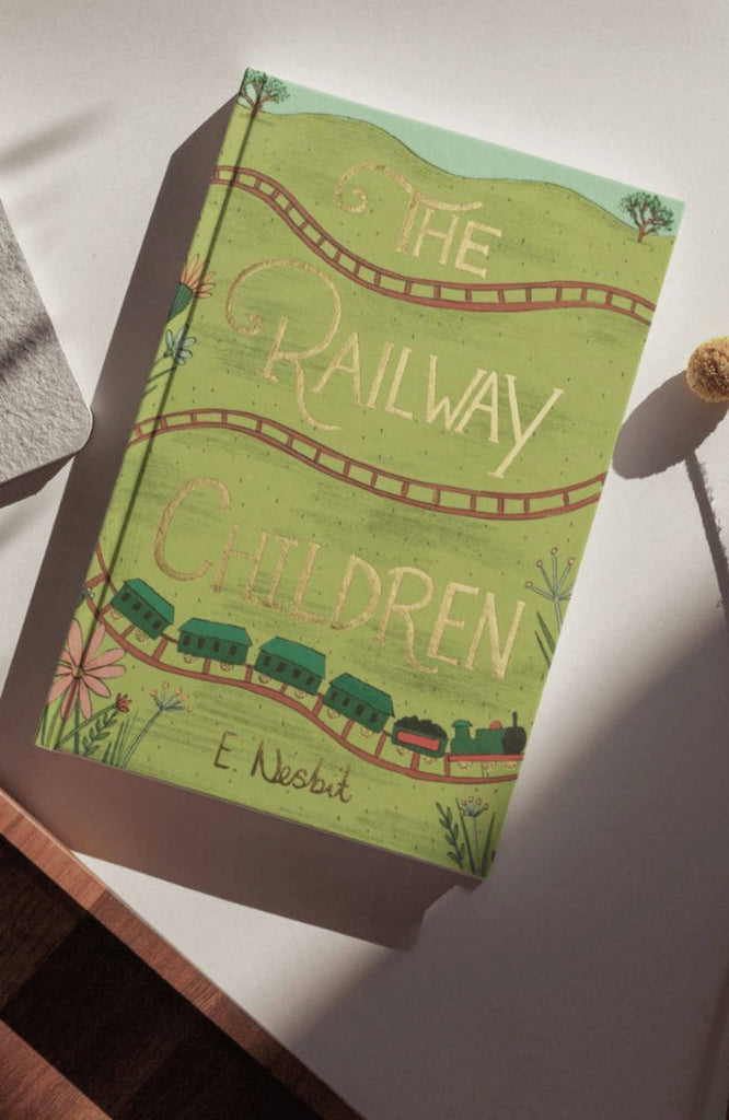 The Railway Children | Collector's Edition | Hardcover features a green cover with illustrated train tracks, a train, and flowers, photographed on a white surface in sunlight.