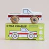 A classic wooden toy truck with red stripes is perched on a green box labeled “No. 30 GT165 Charlie | Made in England.” Crafted from sustainable wood and finished with child-safe paint, this pick-up truck celebrates UK craftsmanship. The box showcases an illustration of the truck, along with icons emphasizing its eco-friendly materials and safety for children.