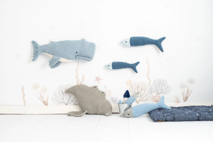 Plush sea creature toys arranged against a wall decorated with underwater illustrations, including a Dark Blue Fish Pack, a dolphin, and coral, on a light background.