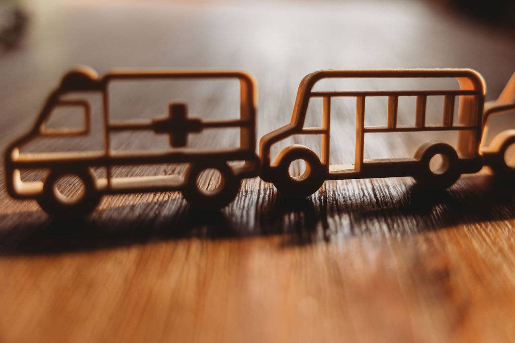 Wooden cutouts of an ambulance and a school bus from our Service Vehicle Cutter Set - Eco Playdough Tool are displayed side by side on a wooden surface, sunlight casting shadows behind them—ideal for sensory play or as eco-friendly playdough tools.