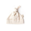 The Organic Baby Hat – Schooner is a soft, cream-colored organic cotton hat featuring a top knot and small sailboat patterns, shown flat on a white background with a side fabric tag—ideal for cozy newborn wear.