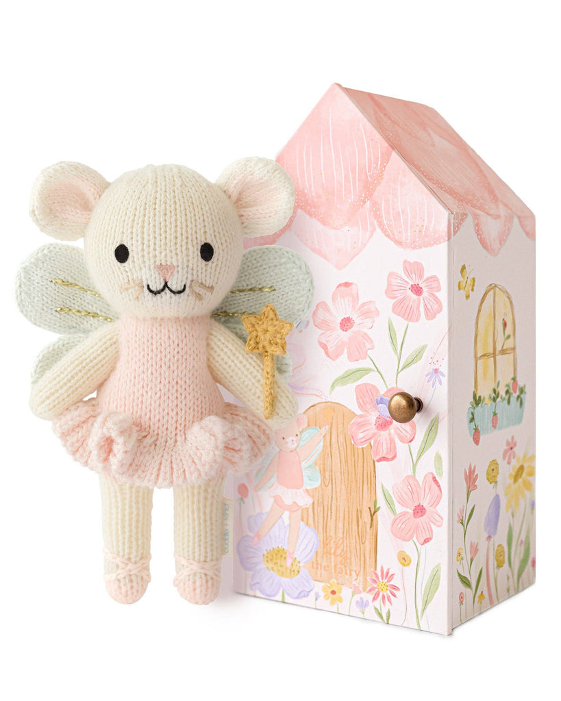 Cuddle + Kind Tiny Lily the Fairy, a hand-knit mouse doll with wings, pink tutu, and star wand, stands beside a pastel house-shaped box decorated with flowers, door, and windows.