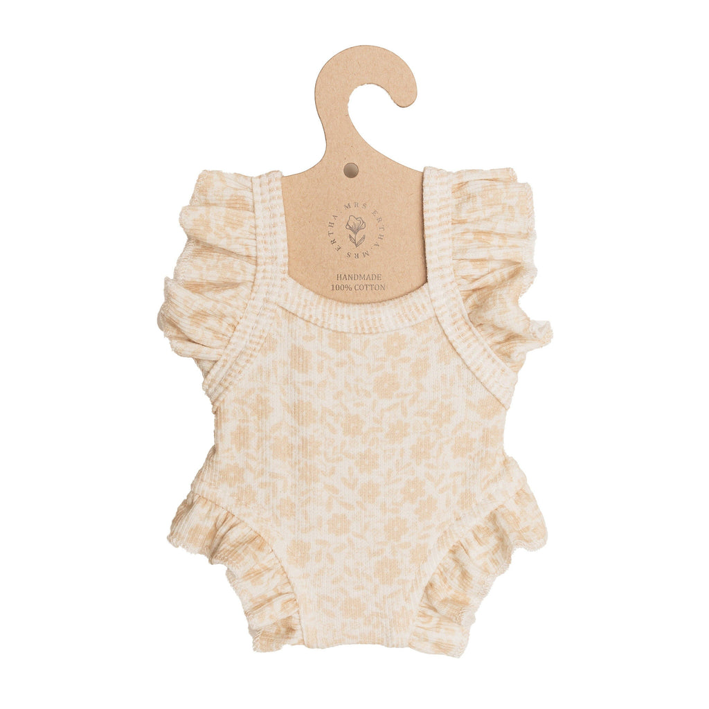 Mrs. Ertha Doll Clothes - 13″-14″ - Bouquet Silhouette Frilled Bodysuit features a cream hue with ruffled sleeves and leg openings, adorned with a delicate floral pattern. Made from 100% organic cotton, this charming bodysuit is displayed on a brown cardboard hanger—perfect as an outfit for Minikane dolls or any 13″-14″ doll collection.