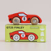 A red wooden racing car with the number 8 on its side rests atop a green box labeled “No. 4 GT25 Finley | Made in England,“ which features an illustration of the car along with icons highlighting sustainability, safety, and English craftsmanship. Its vintage-inspired design captures classic racing style, making it a standout addition to any collection.