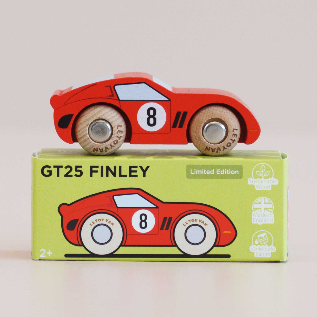 A red wooden racing car with the number 8 on its side rests atop a green box labeled “No. 4 GT25 Finley | Made in England,“ which features an illustration of the car along with icons highlighting sustainability, safety, and English craftsmanship. Its vintage-inspired design captures classic racing style, making it a standout addition to any collection.