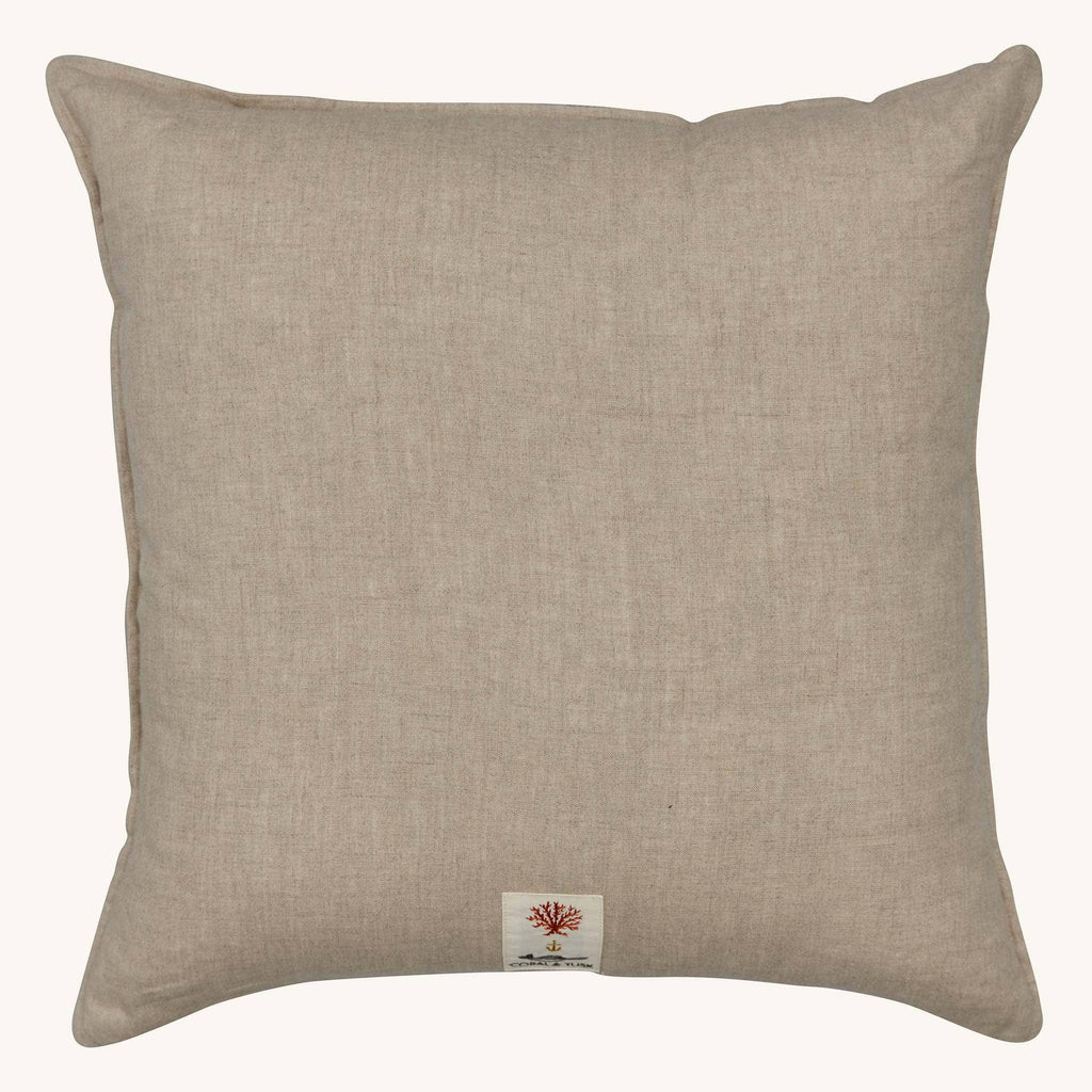 The Coral & Tusk Tree Trimmers Wreath Pillow is a square beige throw pillow with subtle texture and a small fabric tag bearing a tree-like red design—an ideal, understated choice for Christmas decor.