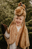 A happy child dressed in the Costume - Brown Horse stands before green pine trees, holding up a hoof-like mitt.