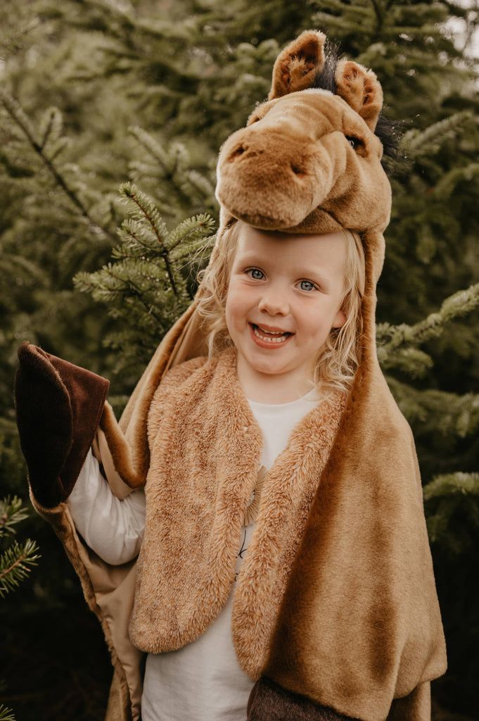 A happy child dressed in the Costume - Brown Horse stands before green pine trees, holding up a hoof-like mitt.