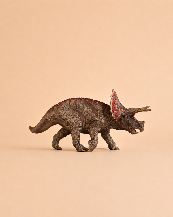 The Schleich Triceratops Dinosaur Toy features a textured brown body with red markings and stands against a plain beige background, making it an ideal educational figurine for collectors and fans of dinosaur toys.