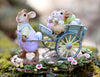 The Wee Forest Folk Tiny Collectible - Easter's on its Way features a hand-sculpted mouse in purple overalls pulling a blue cart with two smaller mice and colorful eggs, surrounded by flowers. Not a toy.