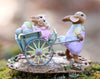 The Wee Forest Folk Tiny Collectible - Easter's on its Way (Not a Toy) is a hand-sculpted miniature featuring a bunny in pastels pushing a blue wheelbarrow with colorful eggs and two small bunnies, set on a floral base.