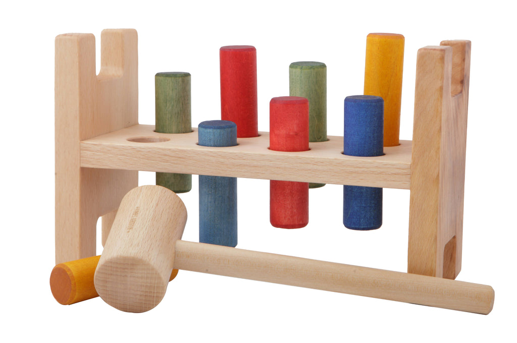 The Rainbow Pound -a- Peg is an eco-friendly wooden Montessori toy featuring colorful pegs and a mallet, designed for children to hammer the pegs through holes in the bench.