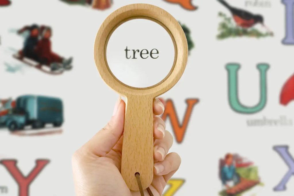 Sentence with replaced product name: A hand holding a Wooden Magnifying Glass over the word "tree" on a colorful educational poster featuring various illustrations and alphabets.