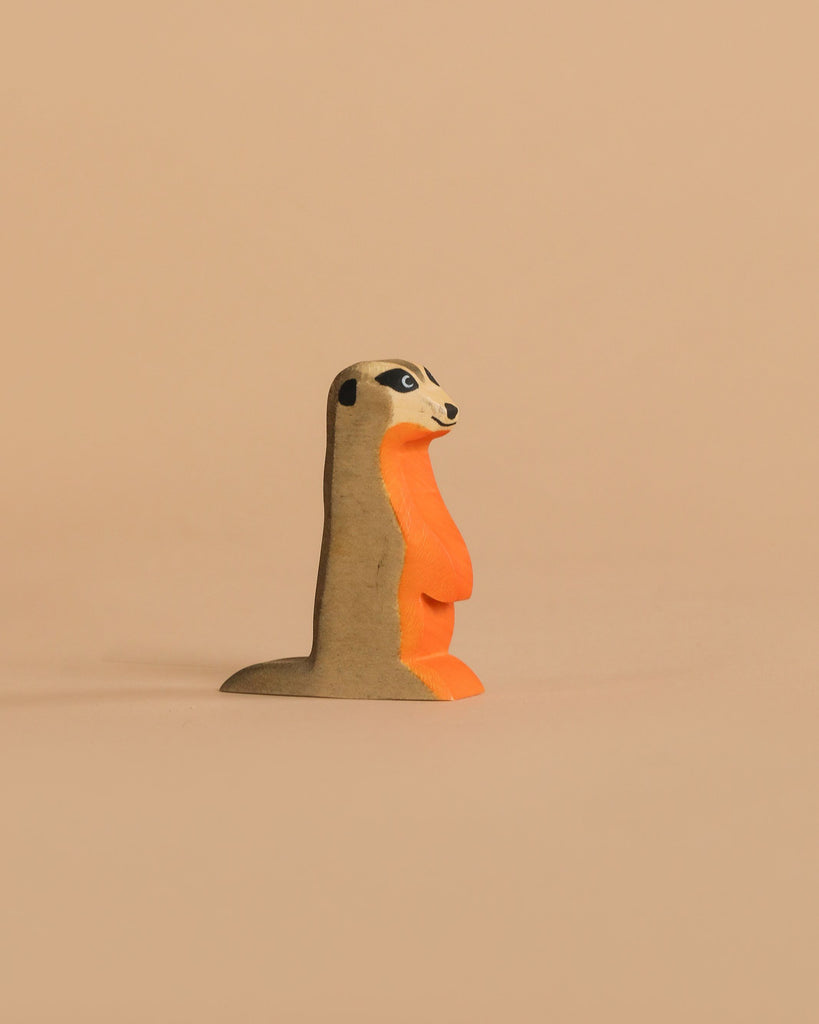 The Handmade Holzwald Meerkat is a small, upright wooden figurine in orange and brown with detailed facial and body accents, photographed against a beige background—an eco-friendly and charming addition to any toy collection.