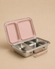A rectangular stainless steel lunch box from Haps Nordic with two compartments and a hinged blush (pink) lid is shown open on a beige surface.