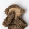 A Slumberkins Bigfoot Snuggler + Intro Book - Self Esteem resembling Bigfoot with its face covered by tan fabric, resembling a face mask, against a light gray background. The bear's small black eyes peek out.