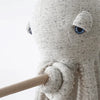 A close-up of the BigStuffed Octopus - Big Original, a gray and speckled soft toy with blue eyes. One of its tentacles holds a wooden stick against a plain white background. This stuffed octopus is ready to explore an underwater world, adding oceanic charm to any room. Ships in approximately one week.