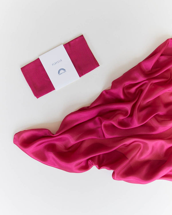 A folded Sarah's Silks Solid Color Playsilk in Red Violet with a white label sits beside a larger piece of matching sheer fabric on a white surface—perfect for open-ended play.