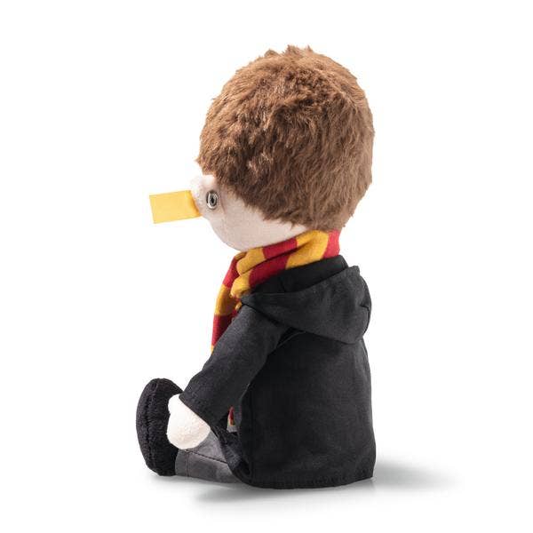 The Steiff Harry Potter Plush 11" features light skin, brown hair, a red and yellow scarf, black coat, and a yellow beak-like detail on its nose, sitting sideways against a white background.