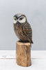 The Hand Carved Ornament - Saw Whet Owl - 10"H is a detailed wooden sculpture with painted feathers, crafted from sustainable softwood, and displayed on a wooden base against a light gray background.