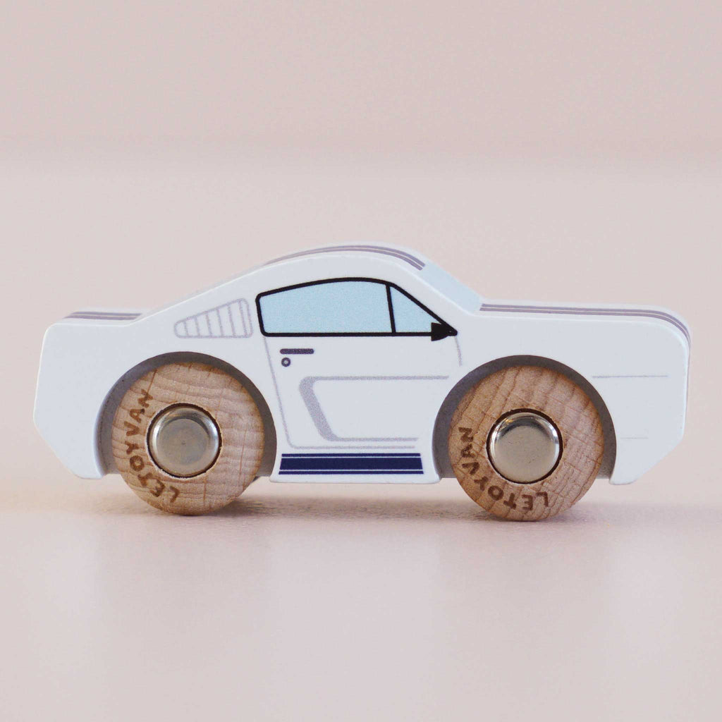 The No. 17 GT95 Maverick, a small white wooden pony car with black and blue detailing and wooden wheels—made in England—is displayed on a light surface against a beige background, evoking the charm of an American classic toy.