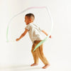 A young boy happily playing with Sarah's Silk Robin's Egg Blue Streamer Wand, twirling it around his body in a bright, neutral-toned studio setting.