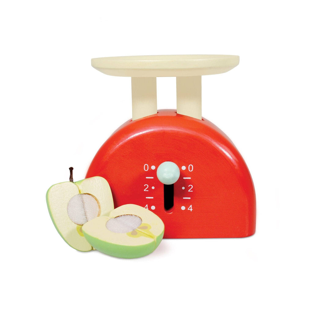 A red wooden Kitchen Weighing Scales with a cream top and dial, ideal for pretend play, is placed next to a sliced wooden toy apple revealing seeds and core details.