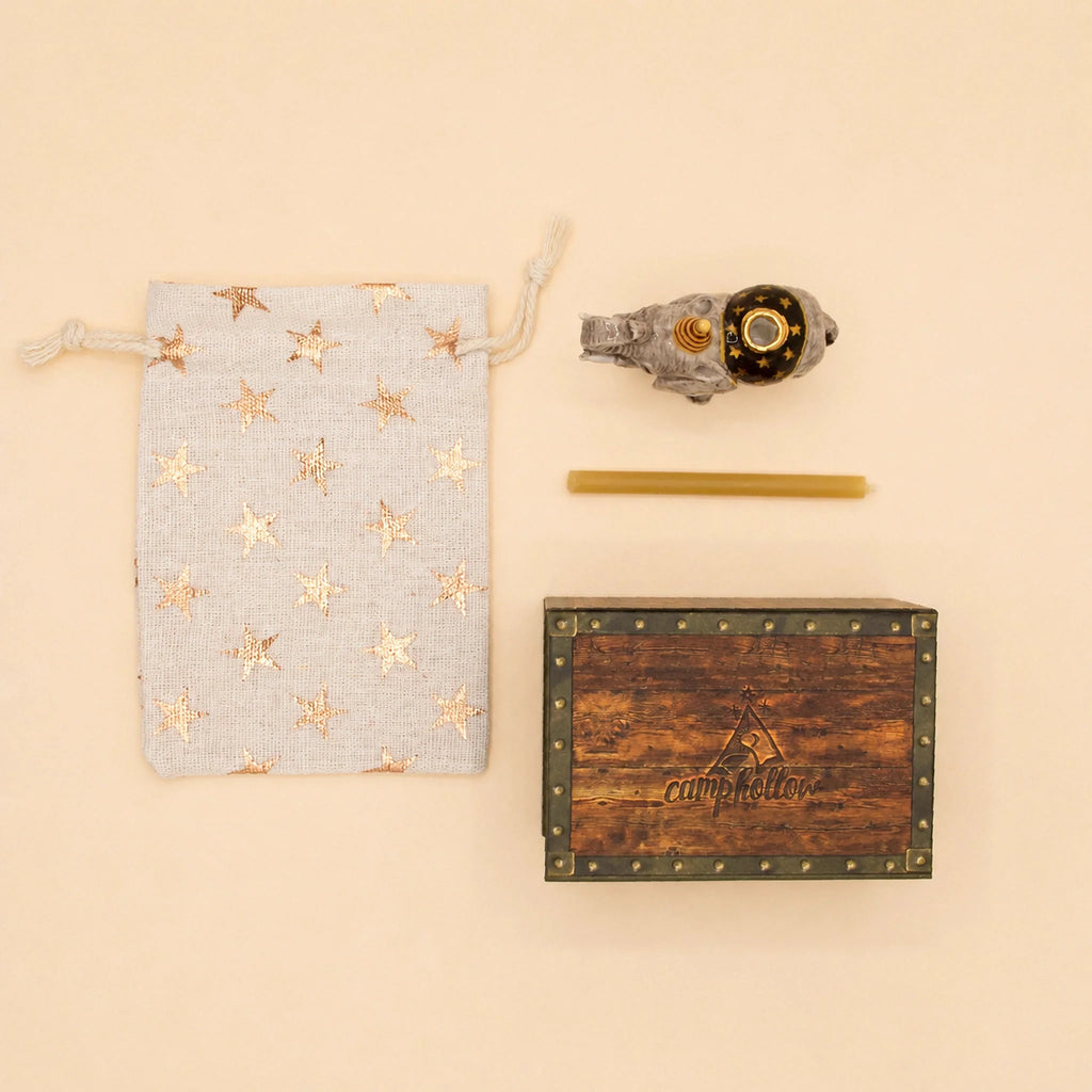 A star-patterned drawstring pouch, a gold pen, an Elephant Cake Topper - Final Sale (ships in one week), and a wooden box labeled “camptellow” are arranged neatly on a beige background.