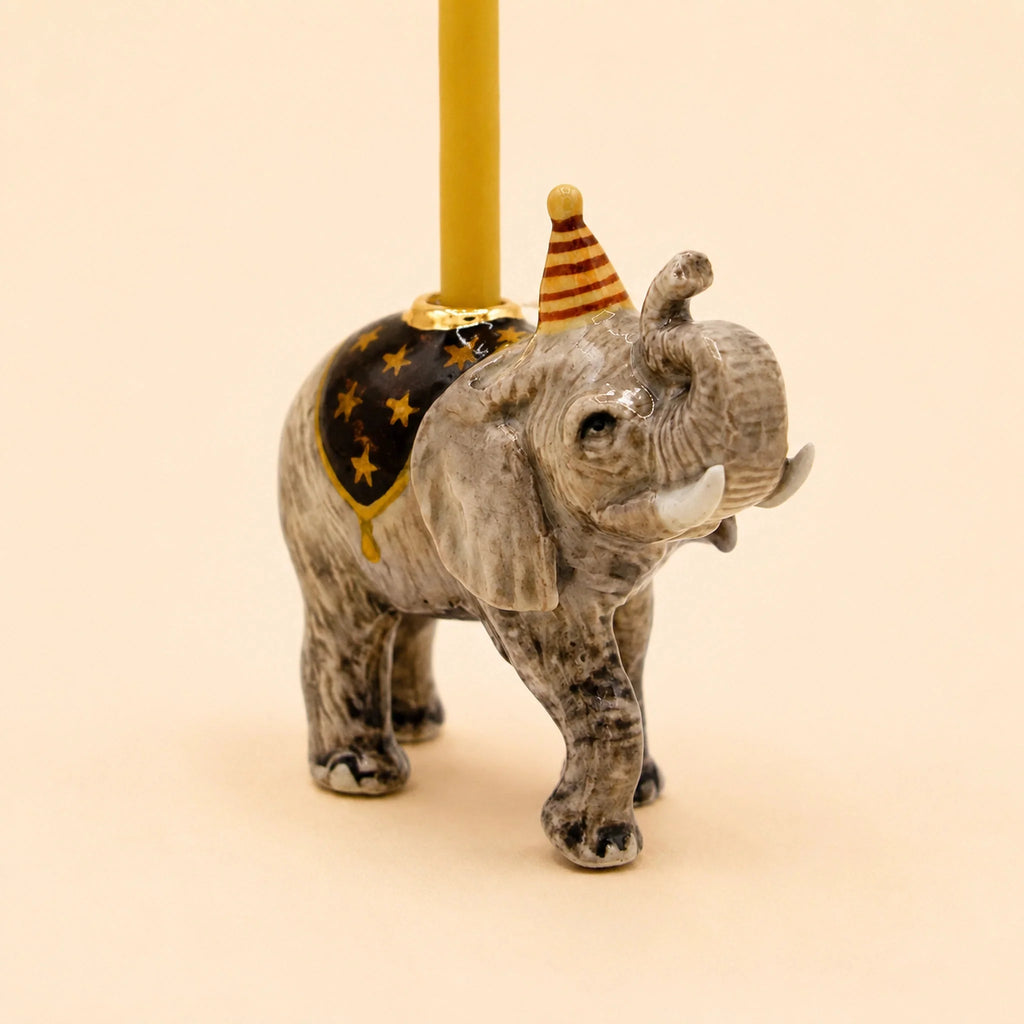 The Elephant Cake Topper - Final Sale (ships in one week) features a hand-painted elephant with a striped party hat, black blanket with gold stars, and a yellow candle—perfect as a collectible keepsake.