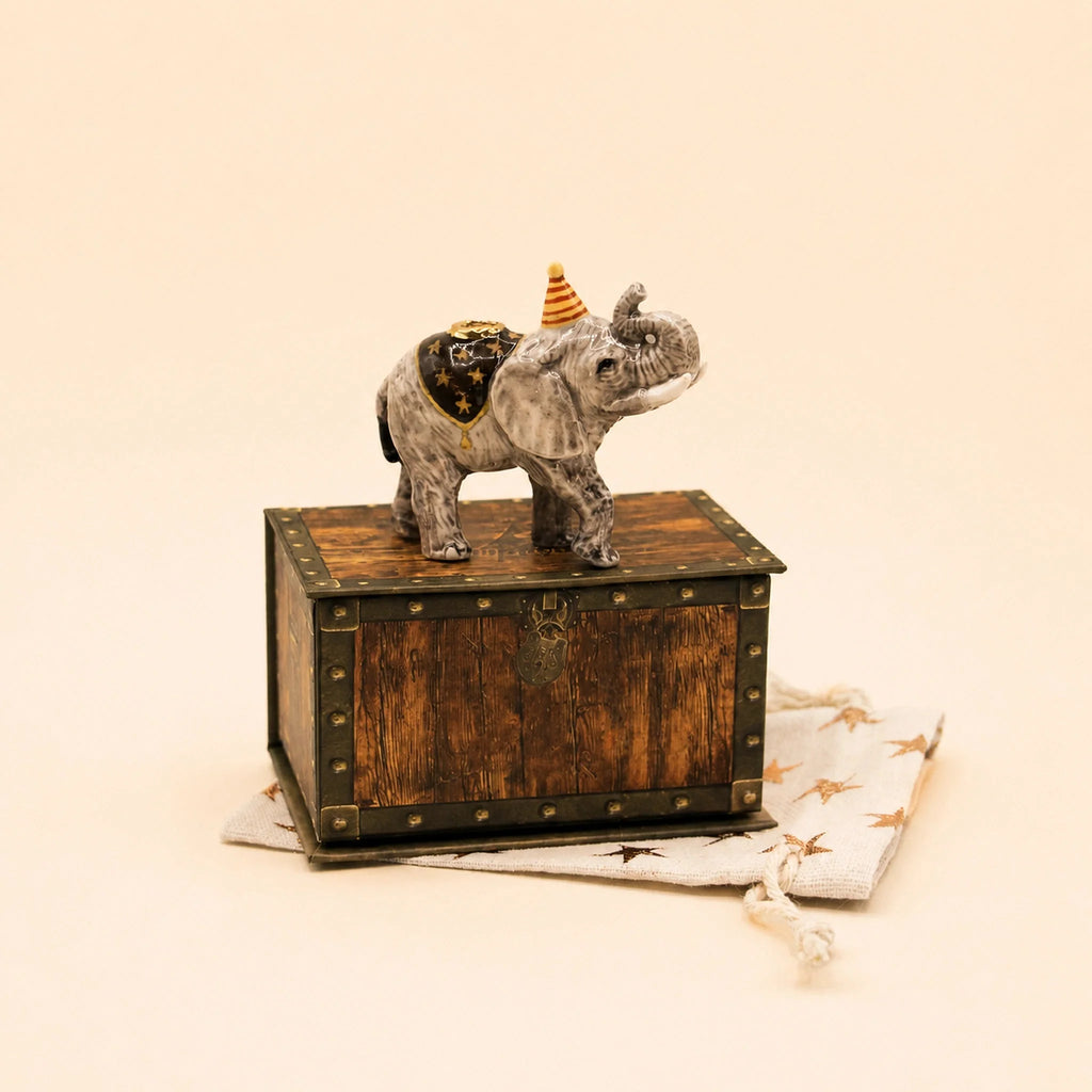 The Elephant Cake Topper - Final Sale (ships in one week) features a hand-painted elephant with a party hat, standing on a vintage wooden box atop a star-patterned fabric pouch—a charming collectible keepsake.