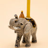 The Elephant Cake Topper - Final Sale (ships in one week) is a small hand-painted ceramic figurine wearing a striped party hat, holding a yellow candle, and featuring detailed accents plus a star-patterned saddle.