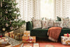 A decorated Christmas tree stands by a green sofa with festive pillows, including the Christmas Wreath Trio Pocket Pillow. Gold and white wrapped gifts sit under the tree, creating a cozy, cheerful holiday atmosphere.